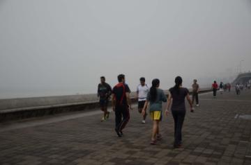 People enjoy their morning walk on a foggy morning at Marine Drive in Mumbai on Jan.21, 2014. (Photo: Sandeep Mahankal/IANS)